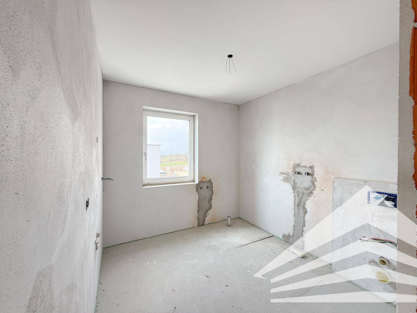 Unfertiges Badezimmer mit vorbereiteten Anschlüssen und einem Fenster für Tageslicht.
