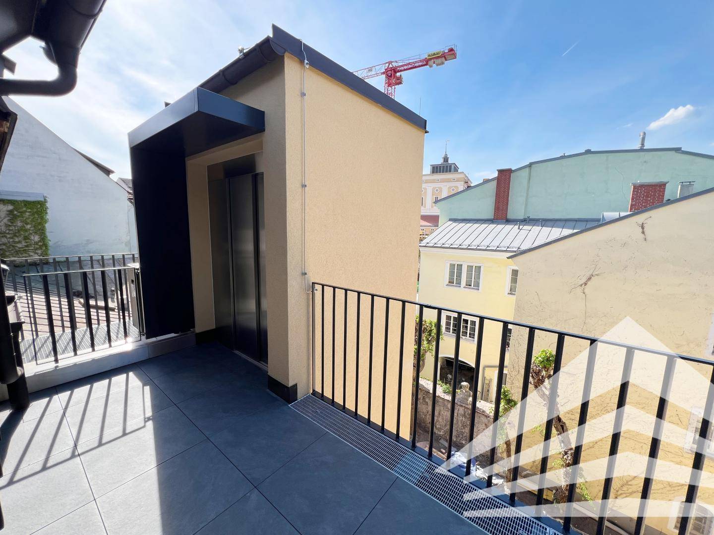 Sonniger Terrassenbereich mit Fliesenboden und Blick auf die Dächer der Nachbargebäude.