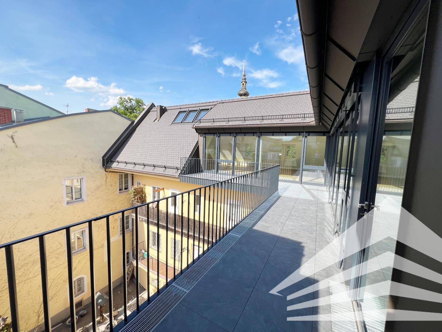Große Dachterrasse mit Fliesenboden, Metallgeländer und Blick auf die umliegenden Gebäude.
