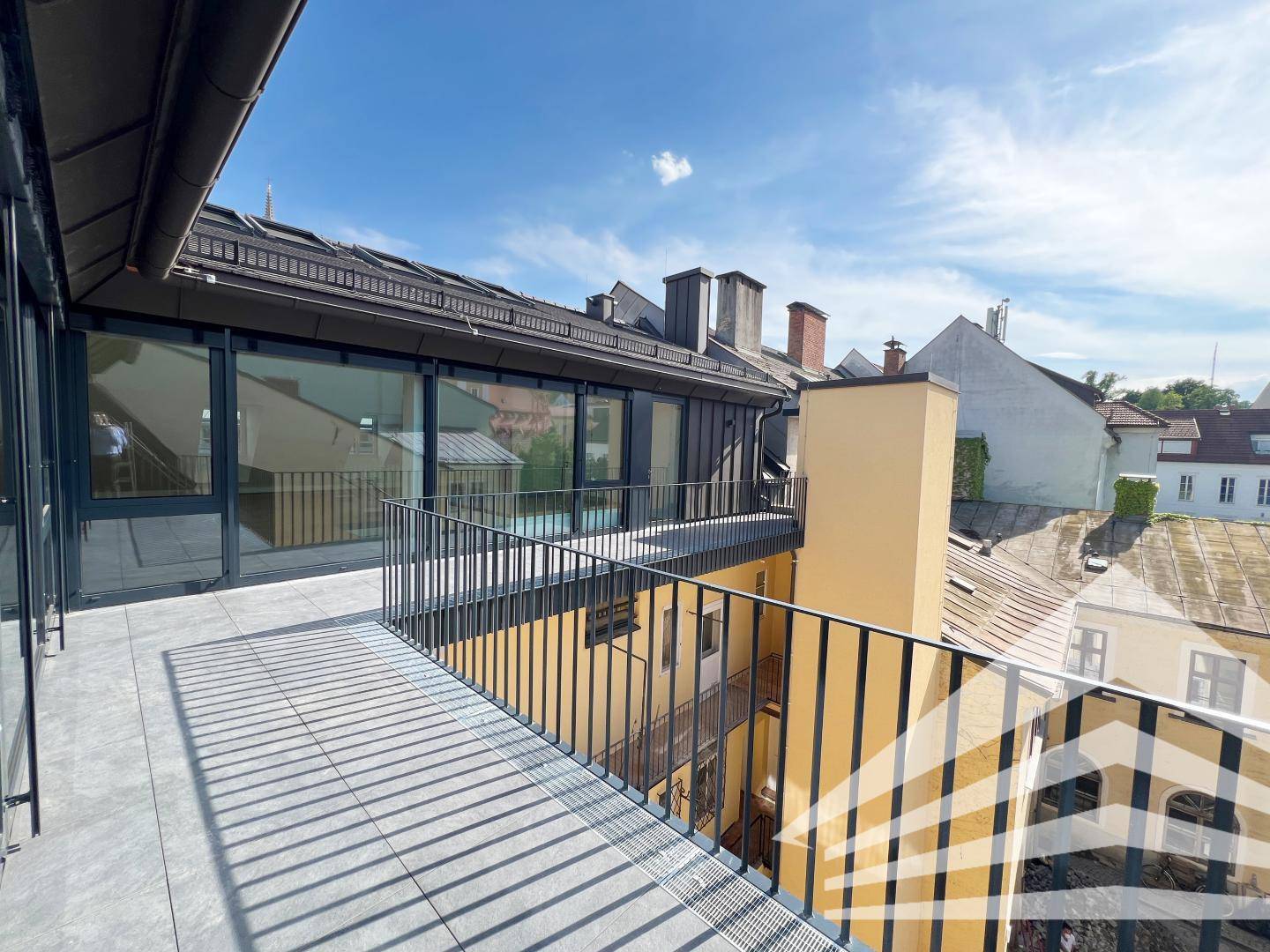 Weitläufige Dachterrasse mit Fliesenboden, schwarzem Geländer und Blick über die Stadt.