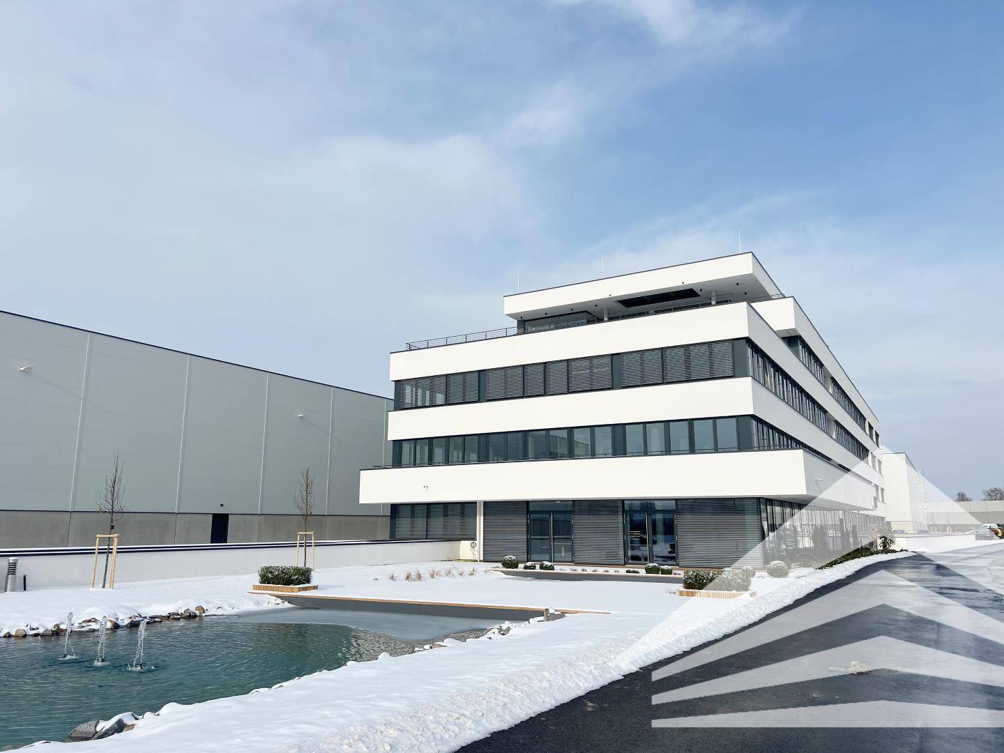 Modernes Bürogebäude mit weißer Fassade, großen Fenstern und Teich im verschneiten Außenbereich.