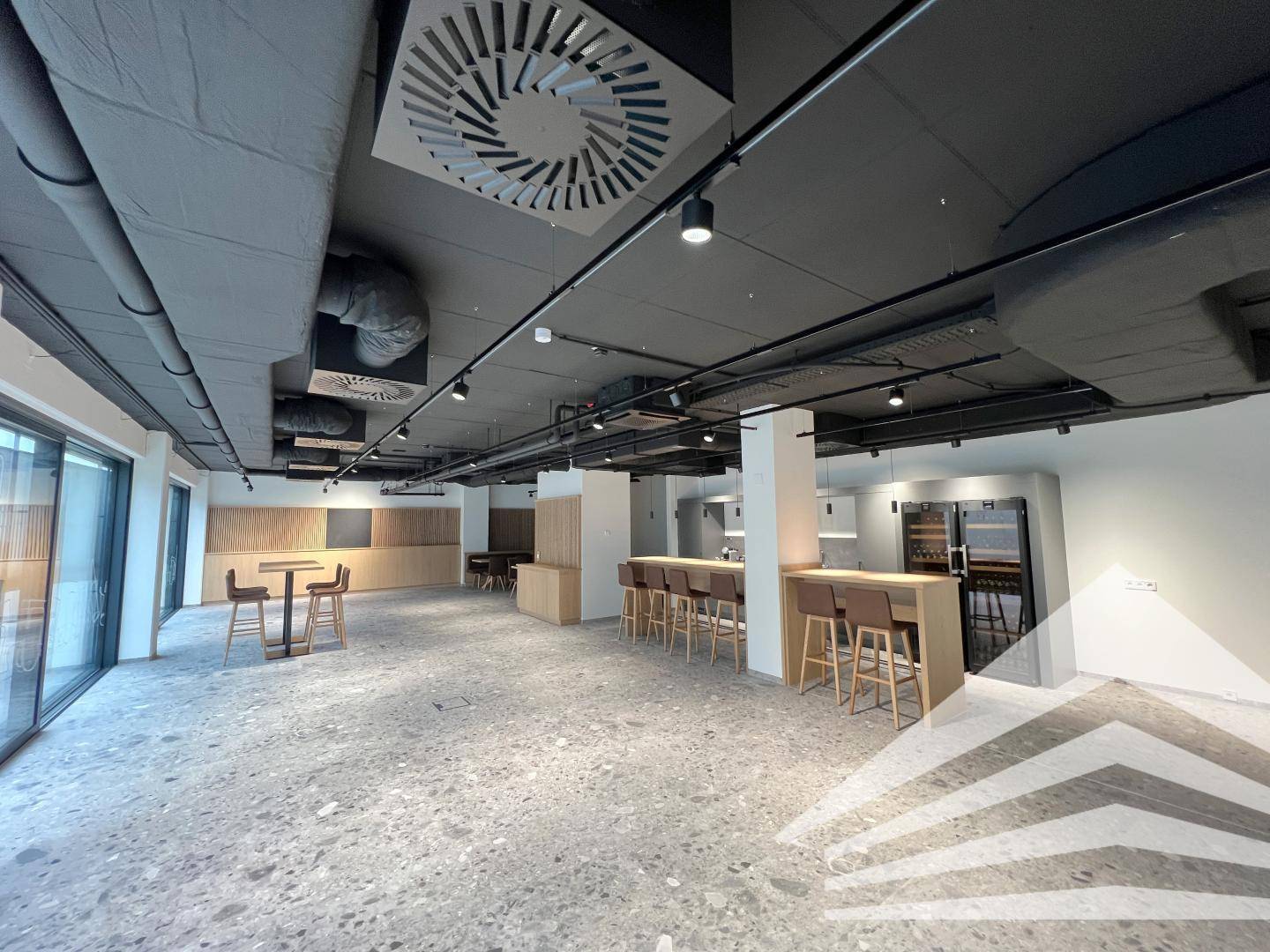 Offener Loungebereich mit Barhockern, hohen Decken und industriellem Design.