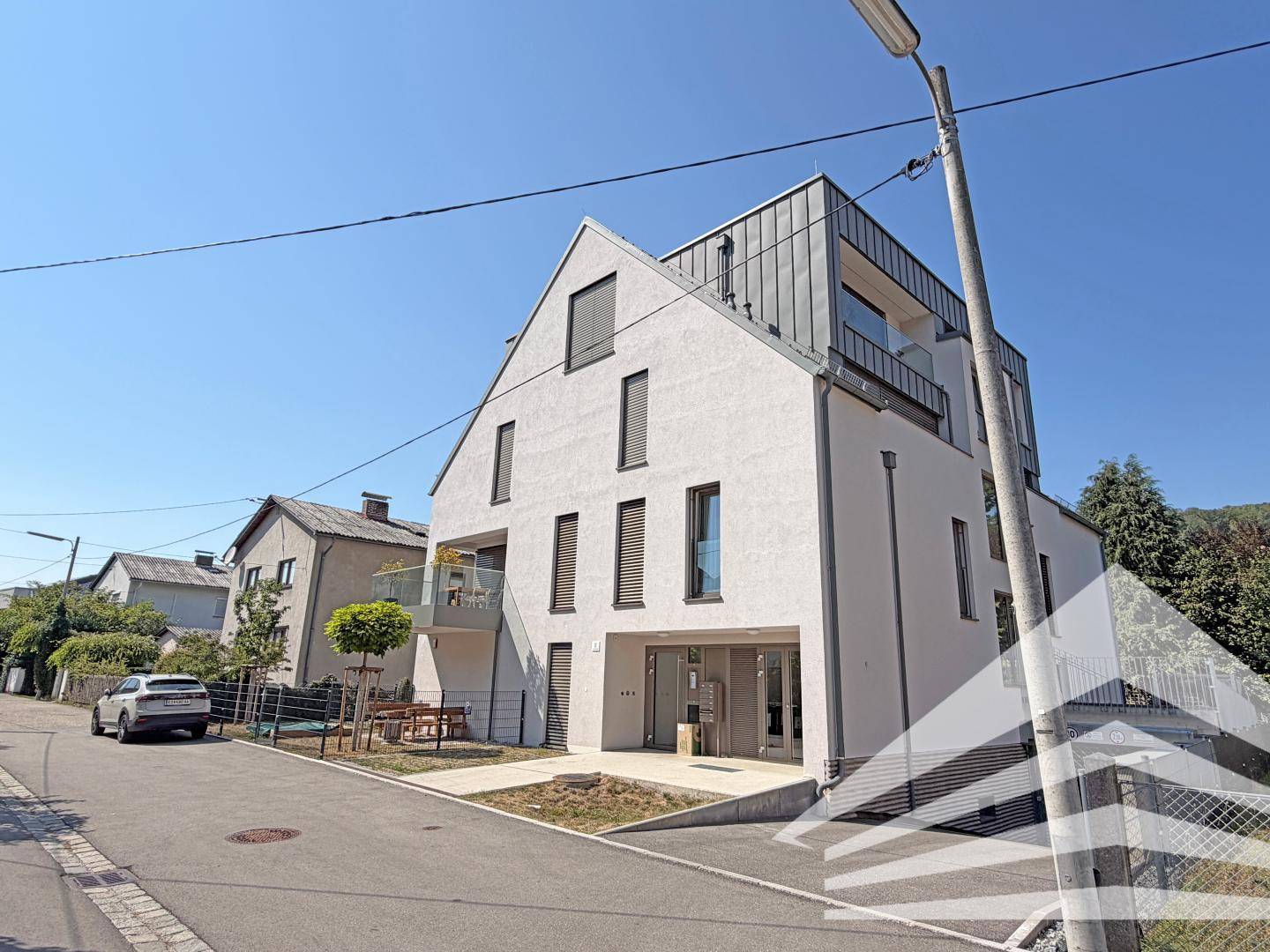 Modernes Mehrfamilienhaus mit weißer Fassade, großen Fenstern und Balkonen.