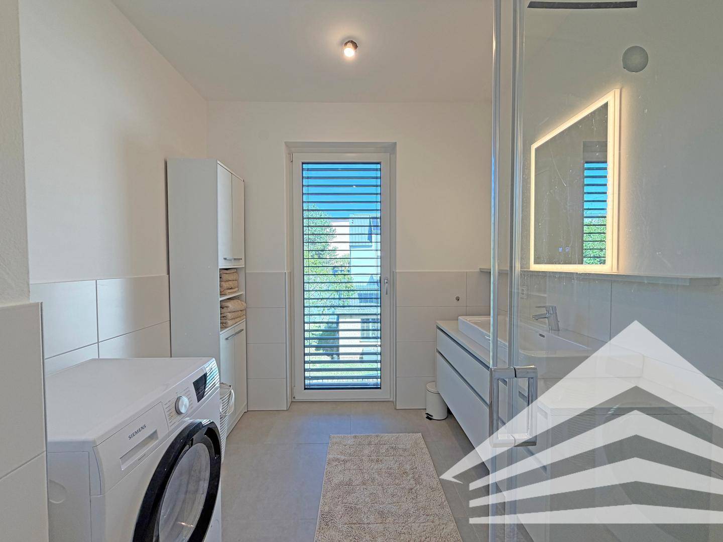 Helles Badezimmer mit Waschmaschine, modernem Waschtisch und großem Fenster.