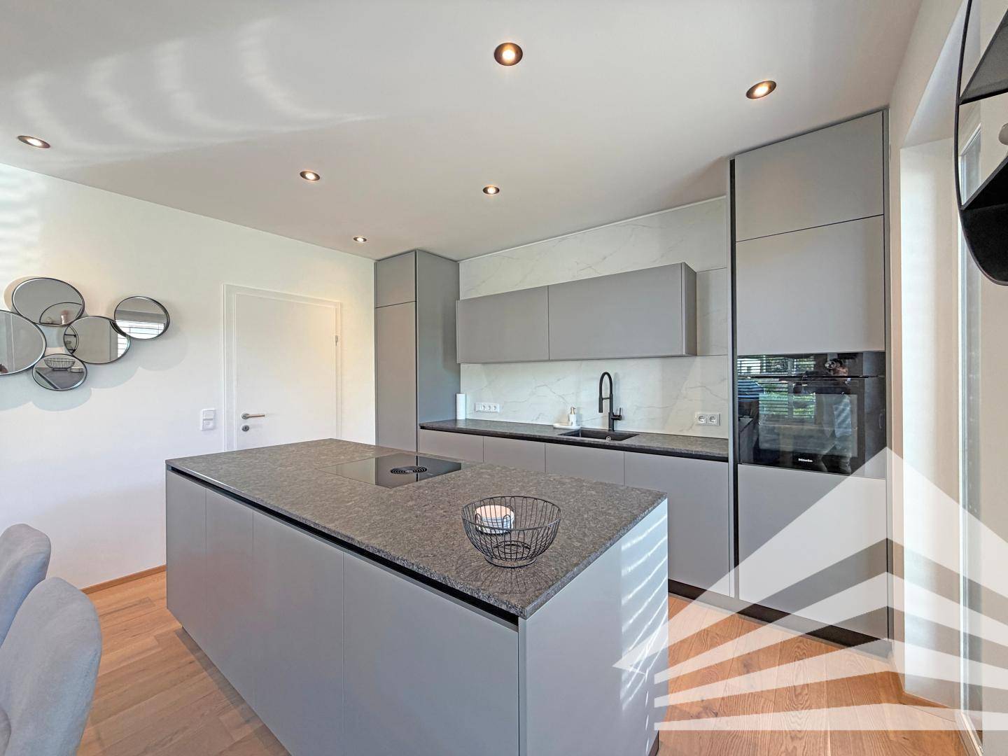Moderne Küche mit Kücheninsel, integriertem Kochfeld und Backofen in zeitgemäßem Design.