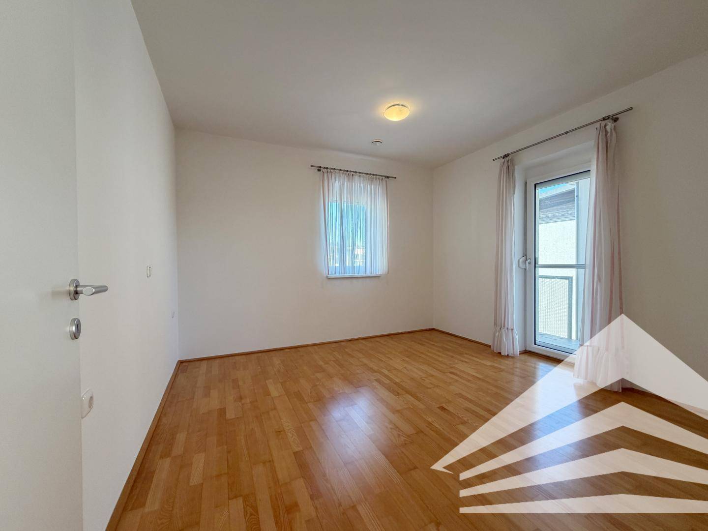 Geräumiges Schlafzimmer mit Holzboden und Fenster, das viel Tageslicht in den Raum lässt.