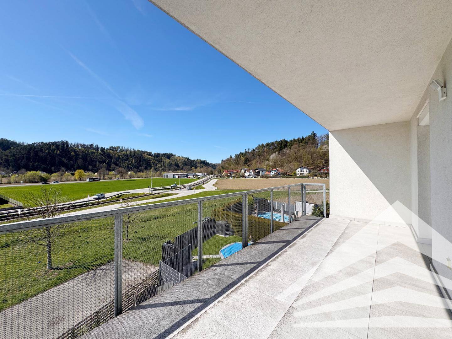Geräumiger Balkon mit Fliesenboden und Glasgeländer, bietet weite Aussicht auf die Landschaft.
