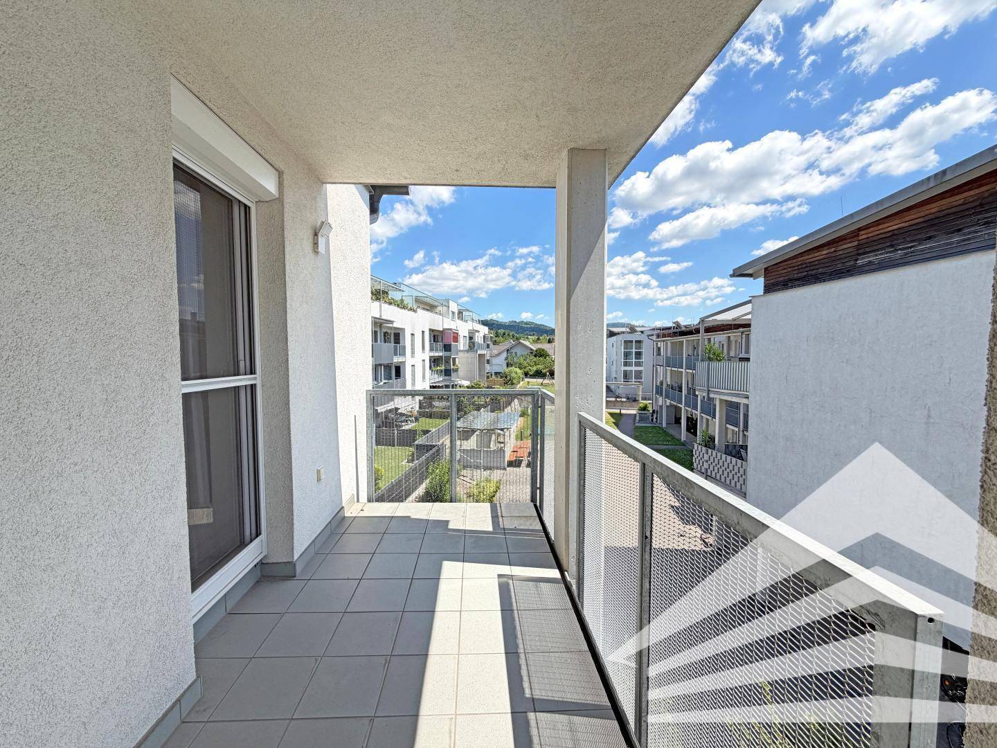 Balkon mit Fliesenboden und Metallgeländer, bietet Blick auf die umliegenden Gebäude und Grünflächen.