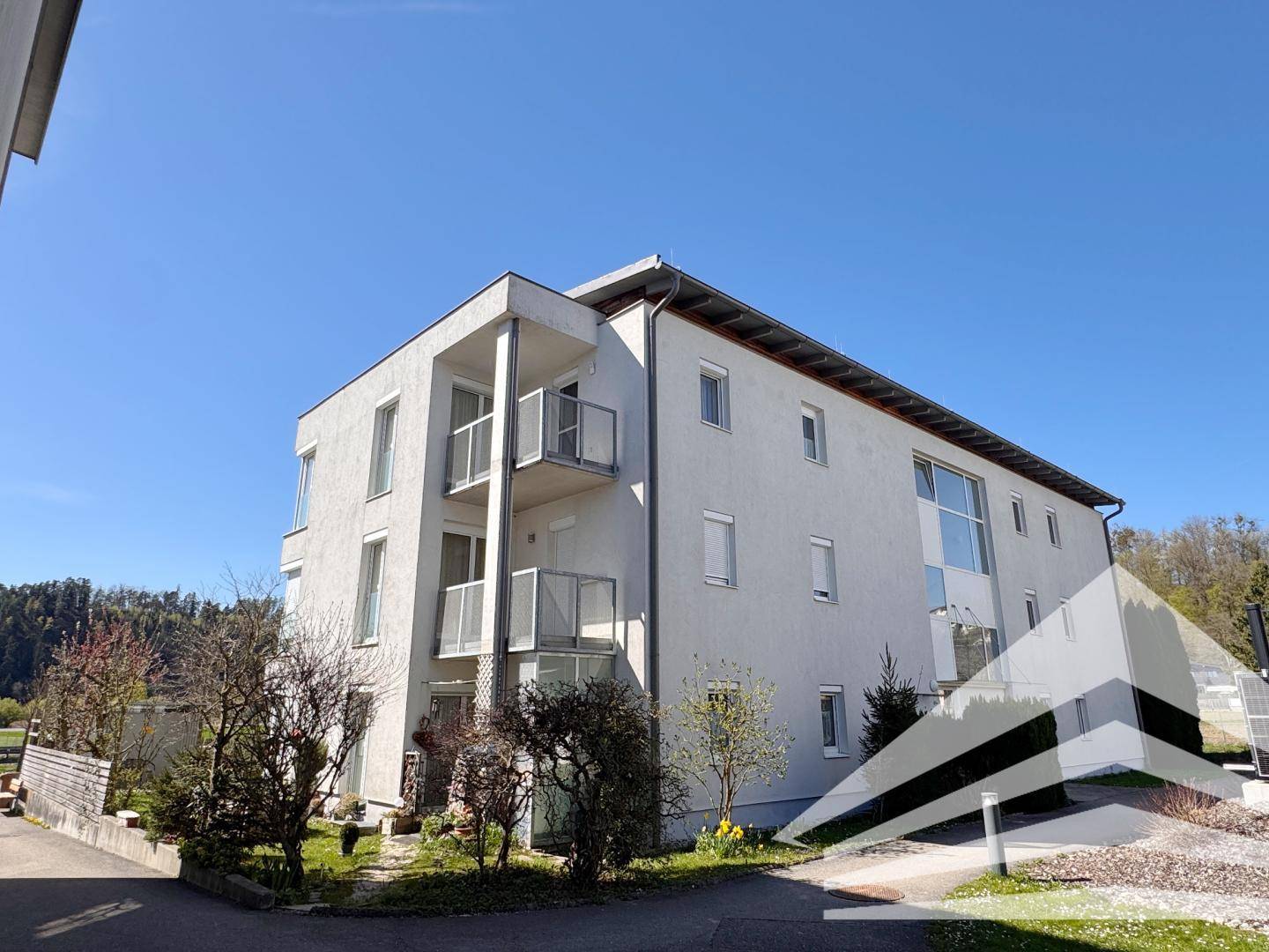 Modernes Mehrfamilienhaus mit weißer Fassade und Balkonen, umgeben von Grünflächen.