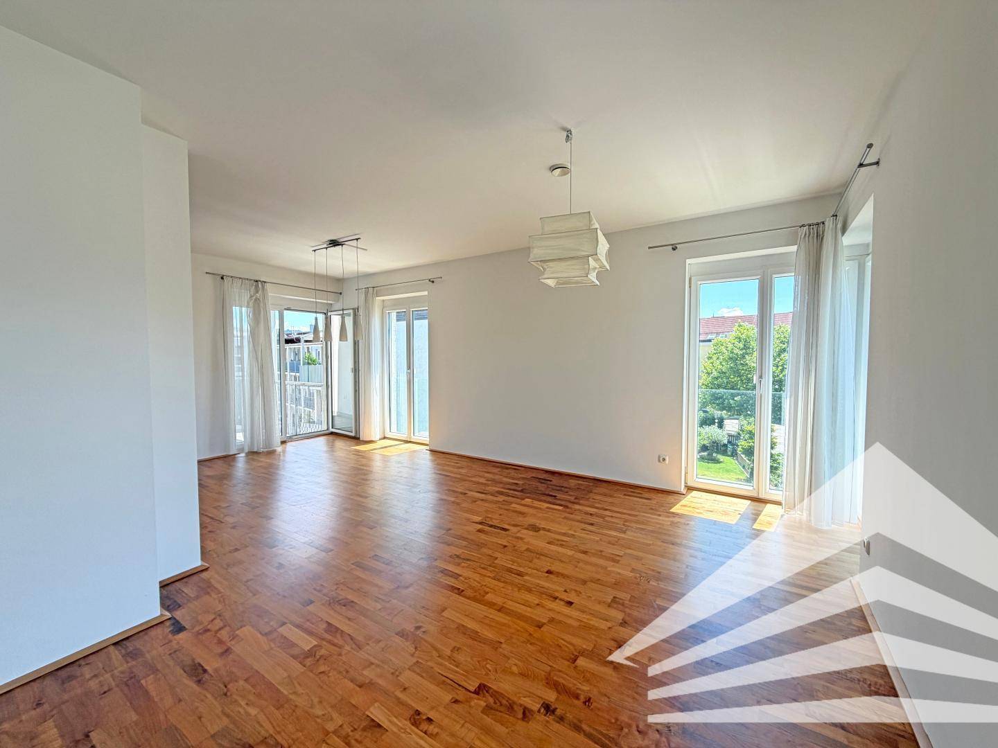 Heller Wohnbereich mit Parkettboden und mehreren Fenstertüren, die viel Tageslicht hereinlassen.
