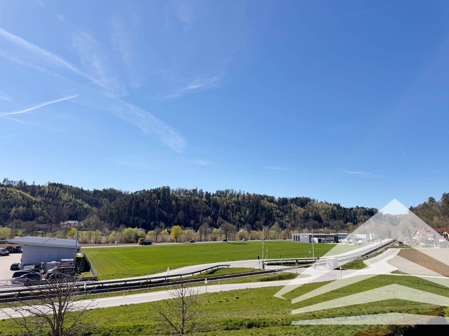 Weitläufige Landschaft mit grünen Feldern und bewaldeten Hügeln unter blauem Himmel.