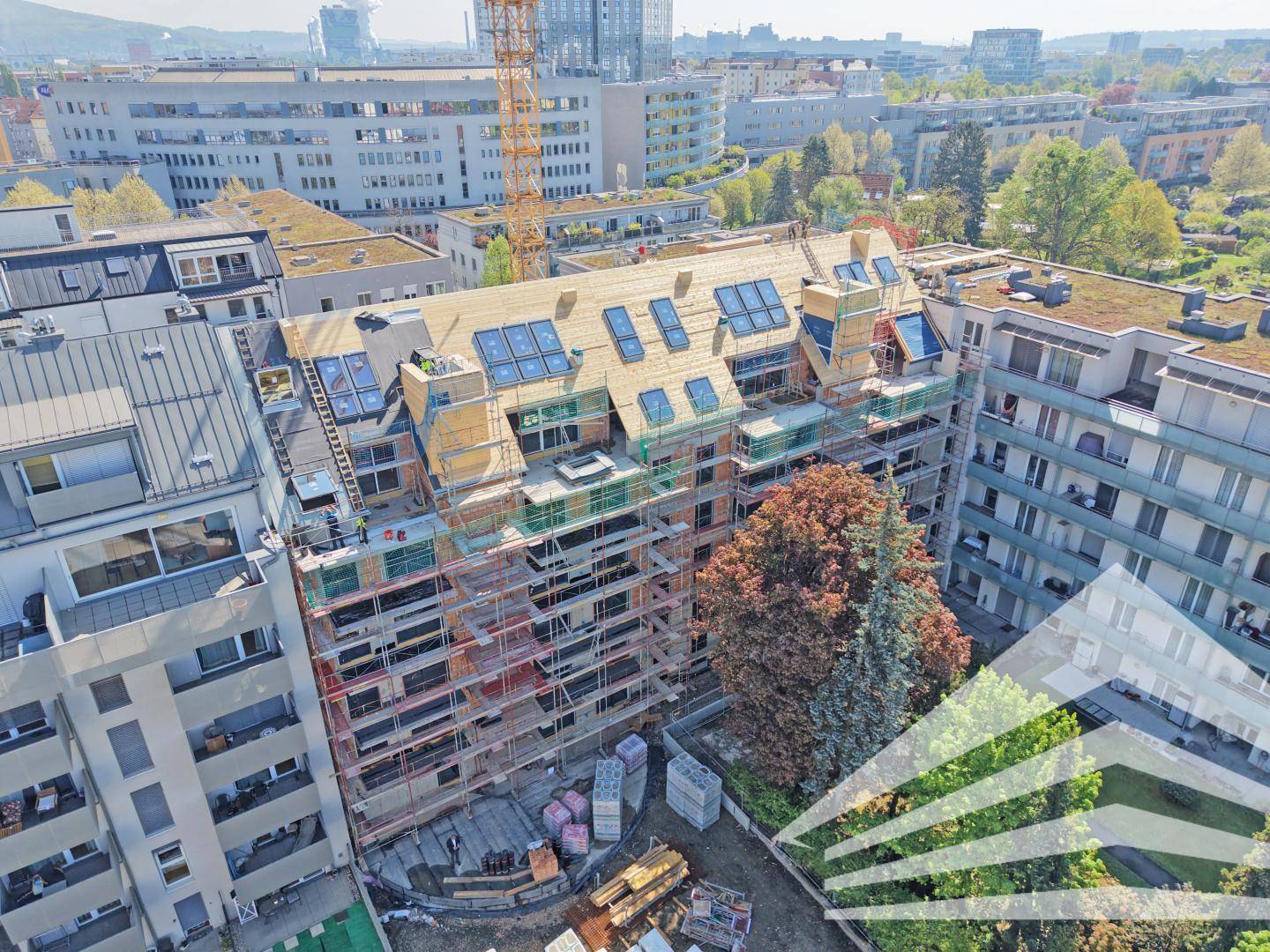 Luftaufnahme eines Neubaus mit Dachfenstern und Solarpaneelen, umgeben von Bäumen und Gebäuden.