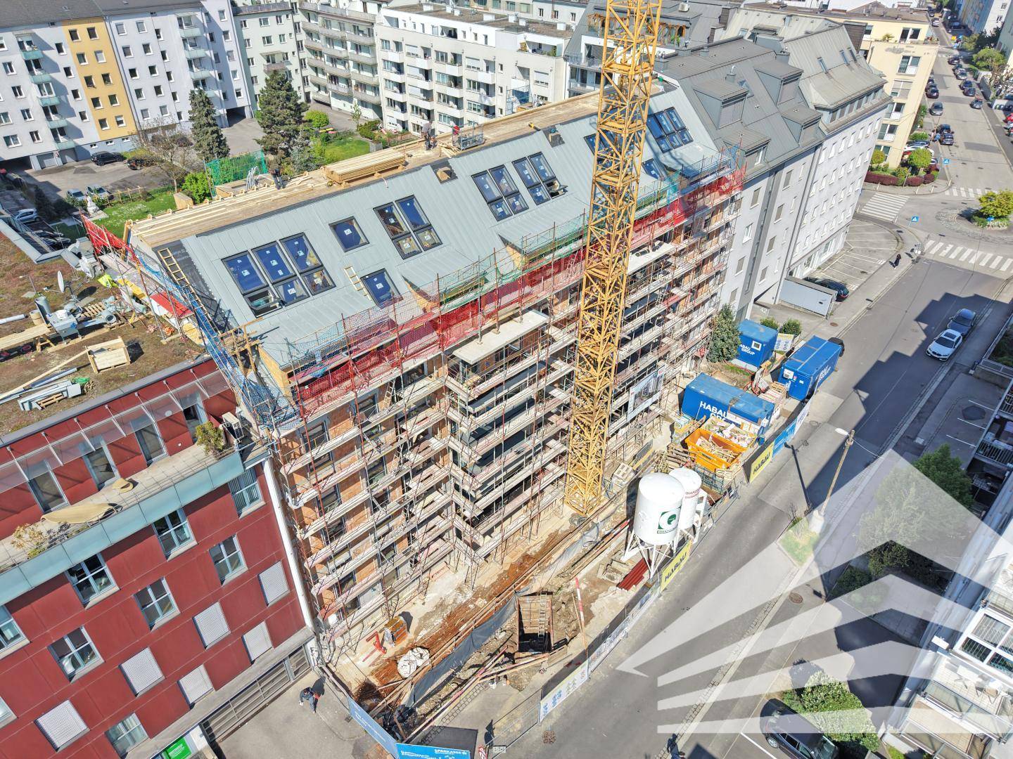 Luftaufnahme eines im Bau befindlichen Gebäudes mit Gerüst und Kran in städtischer Umgebung.