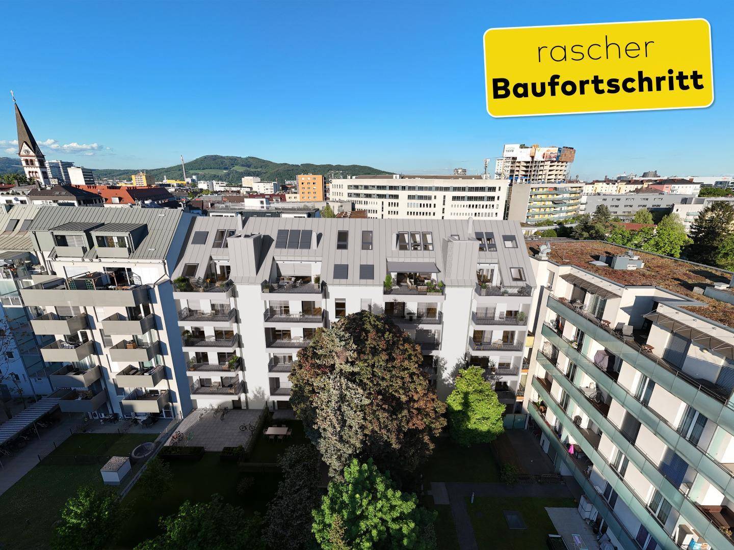 Luftaufnahme einer modernen Wohnanlage bei Tageslicht mit begrüntem Innenhof und Stadtpanorama.