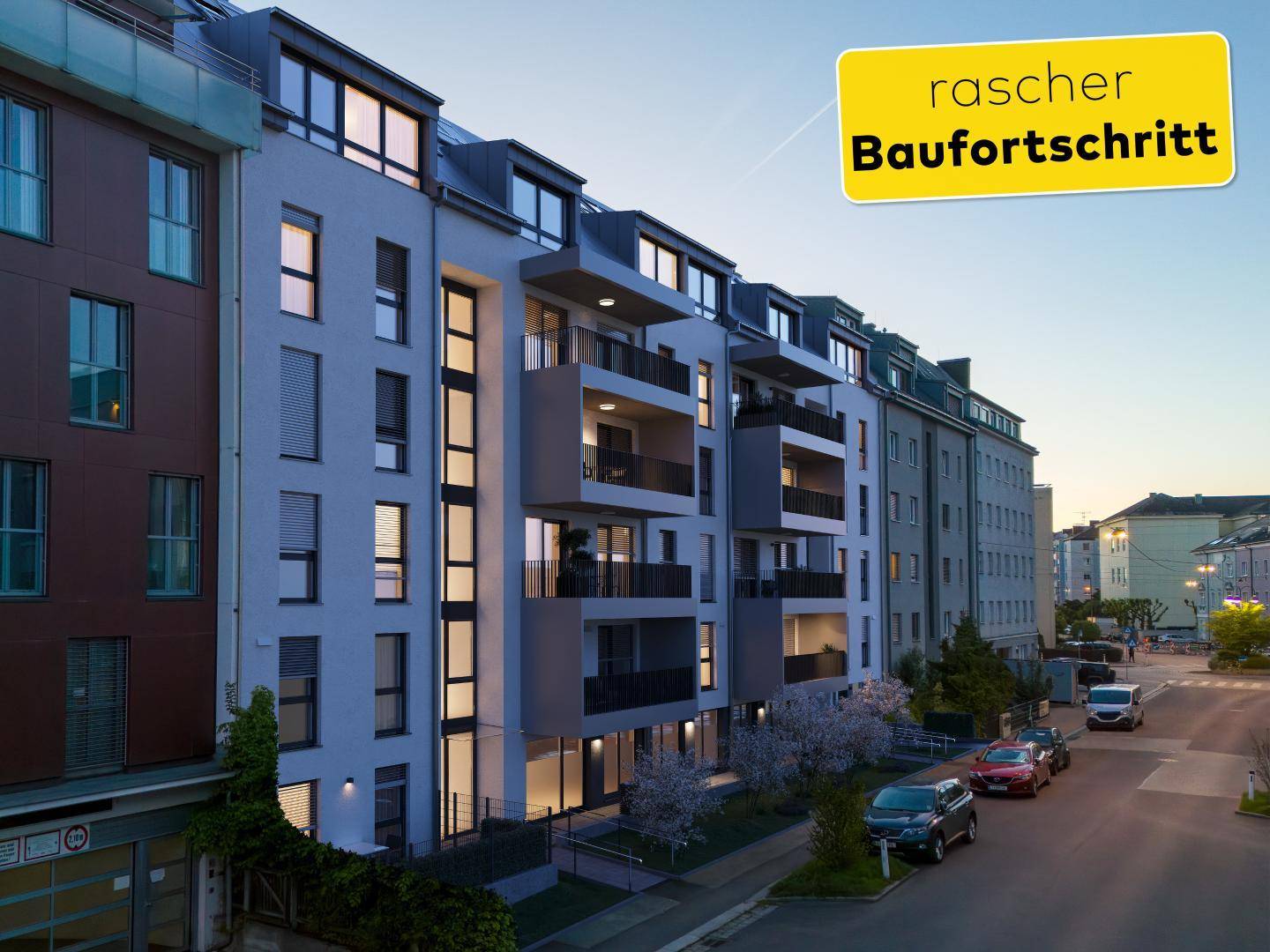 Abendliche Ansicht einer modernen Wohnanlage mit beleuchteten Balkonen und großen Fenstern.