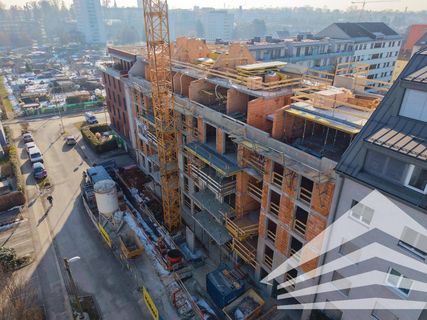 Baustelle eines Wohnkomplexes mit Kran und angrenzender Straße in städtischer Umgebung.