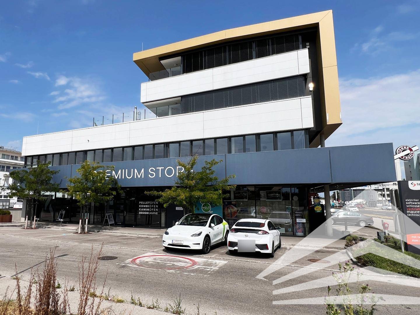 Modernes Geschäftsgebäude mit markanter Architektur, Parkplätzen und Ladestationen für Elektrofahrzeuge.