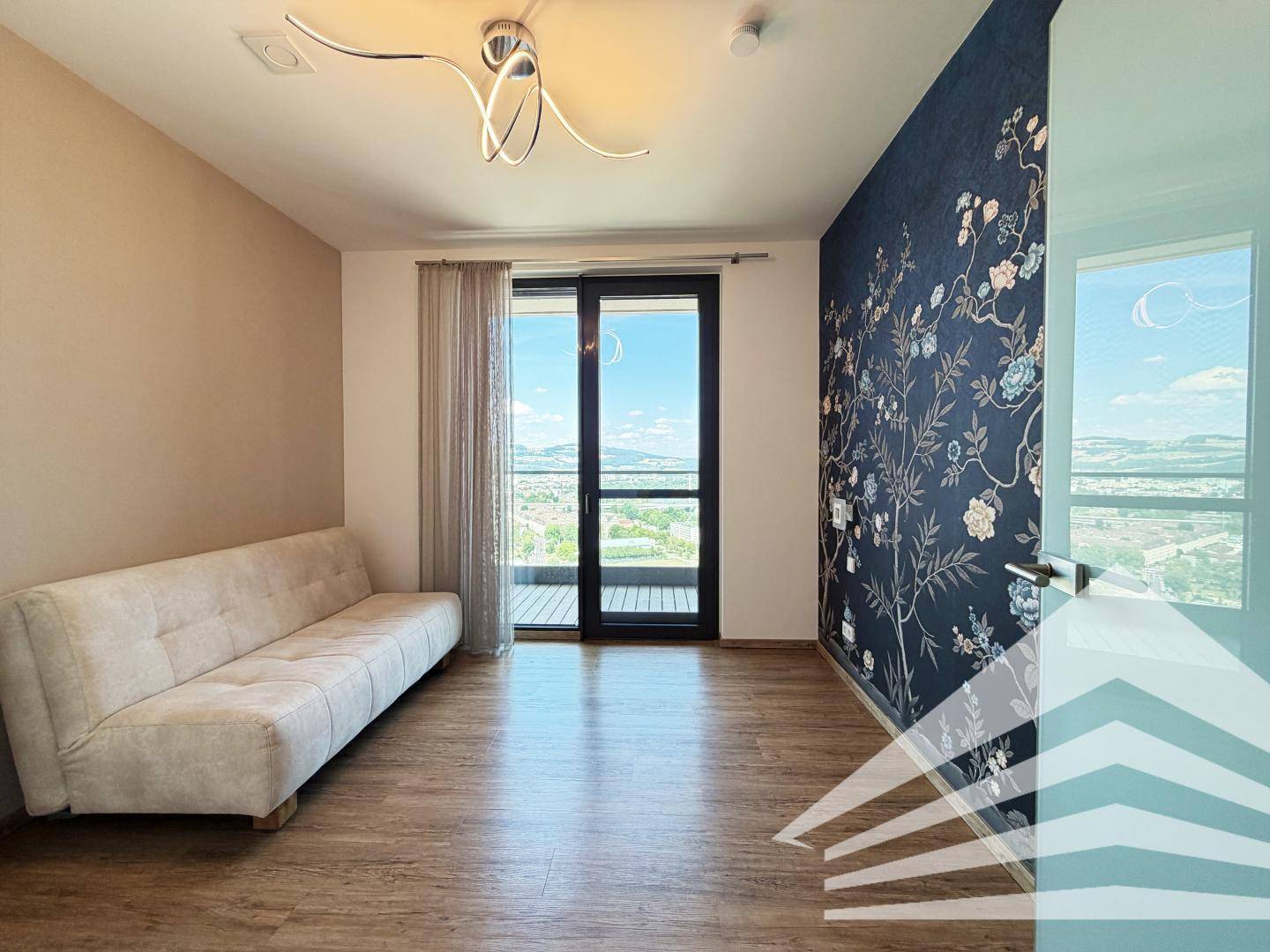 Gemütliches Zimmer mit Sofa, dekorativer Wandtapete und großen Fenstern mit Panoramablick.