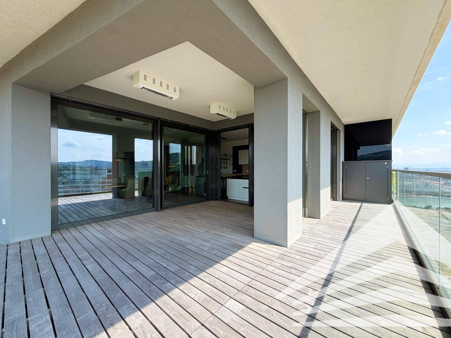 Weitläufige Terrasse mit Holzboden, Glasbrüstung und großen Schiebetüren zum Innenbereich.