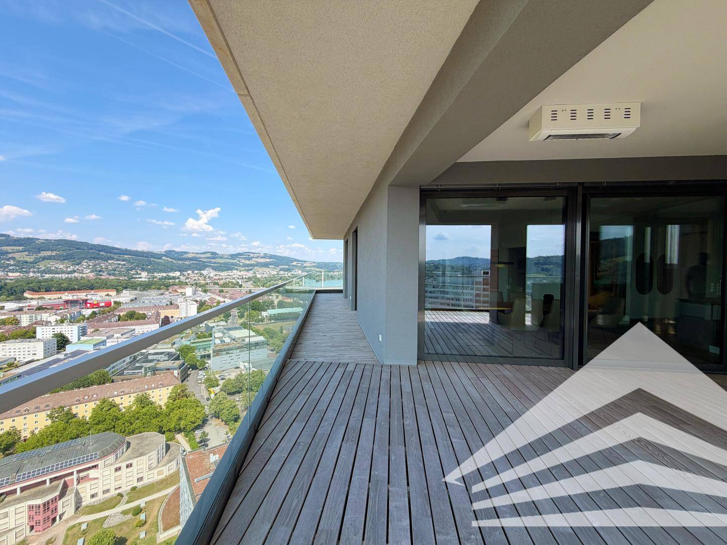 Weitläufige Terrasse mit Holzboden, Glasgeländer und großen Schiebetüren zum Innenbereich.