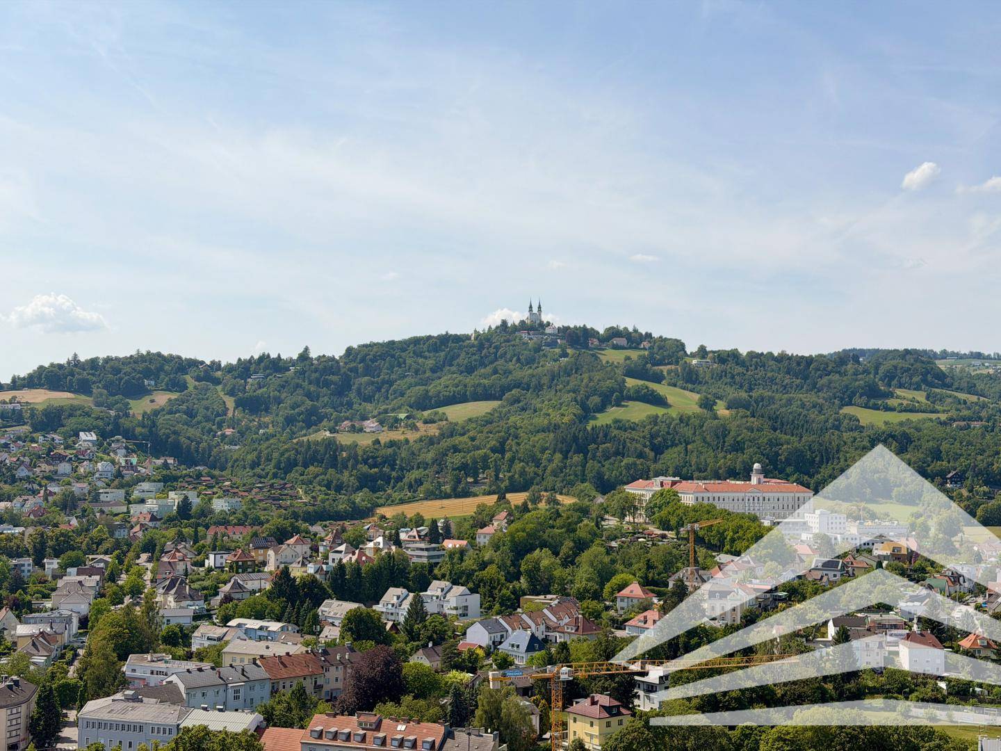 Panoramablick über eine grüne Hügellandschaft mit einer Stadt und einem markanten Gebäude auf dem Gipfel.
