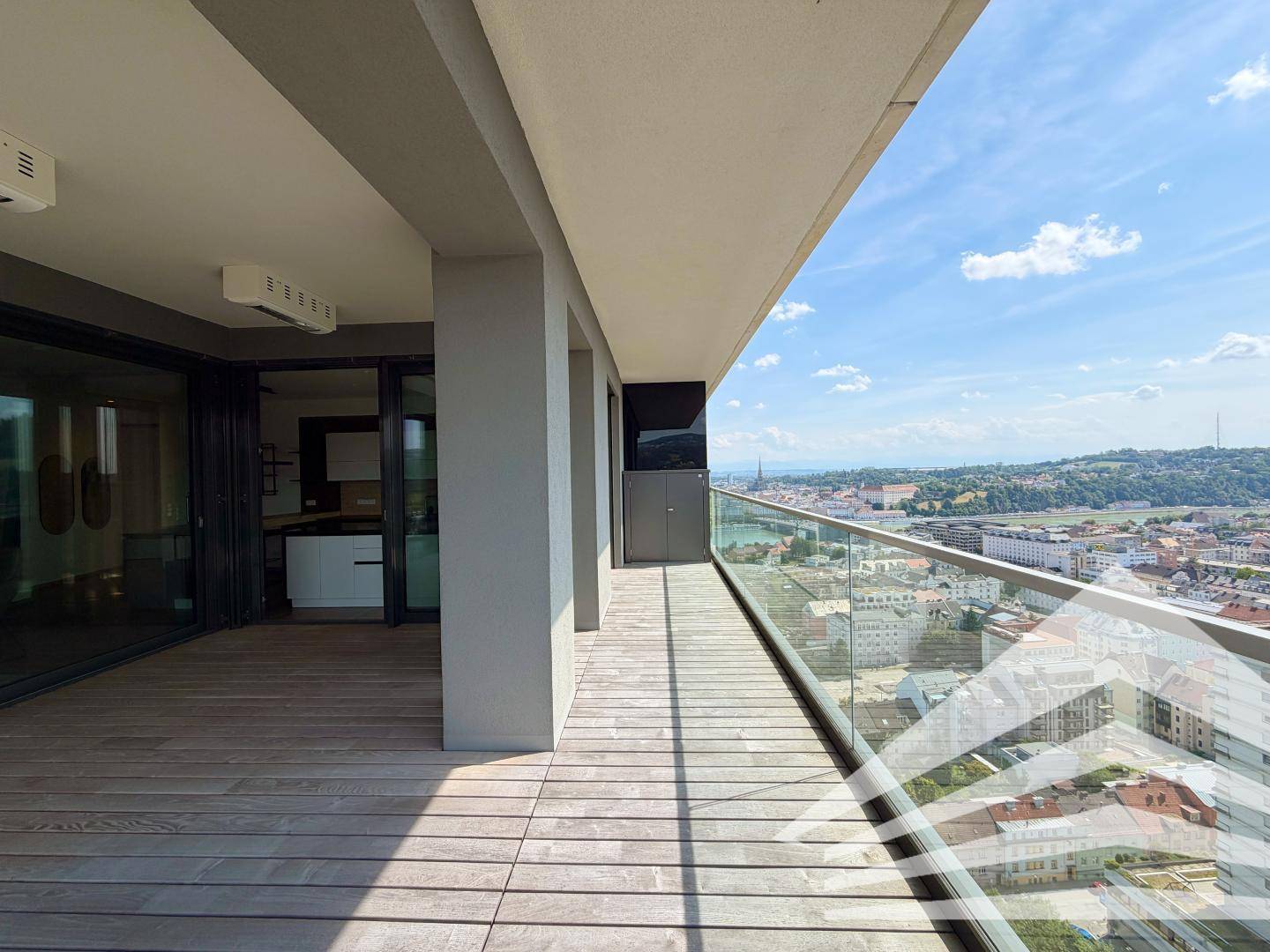 Langer Terrassenbereich mit Holzboden und Glasgeländer, der einen weiten Blick über die Stadt bietet.