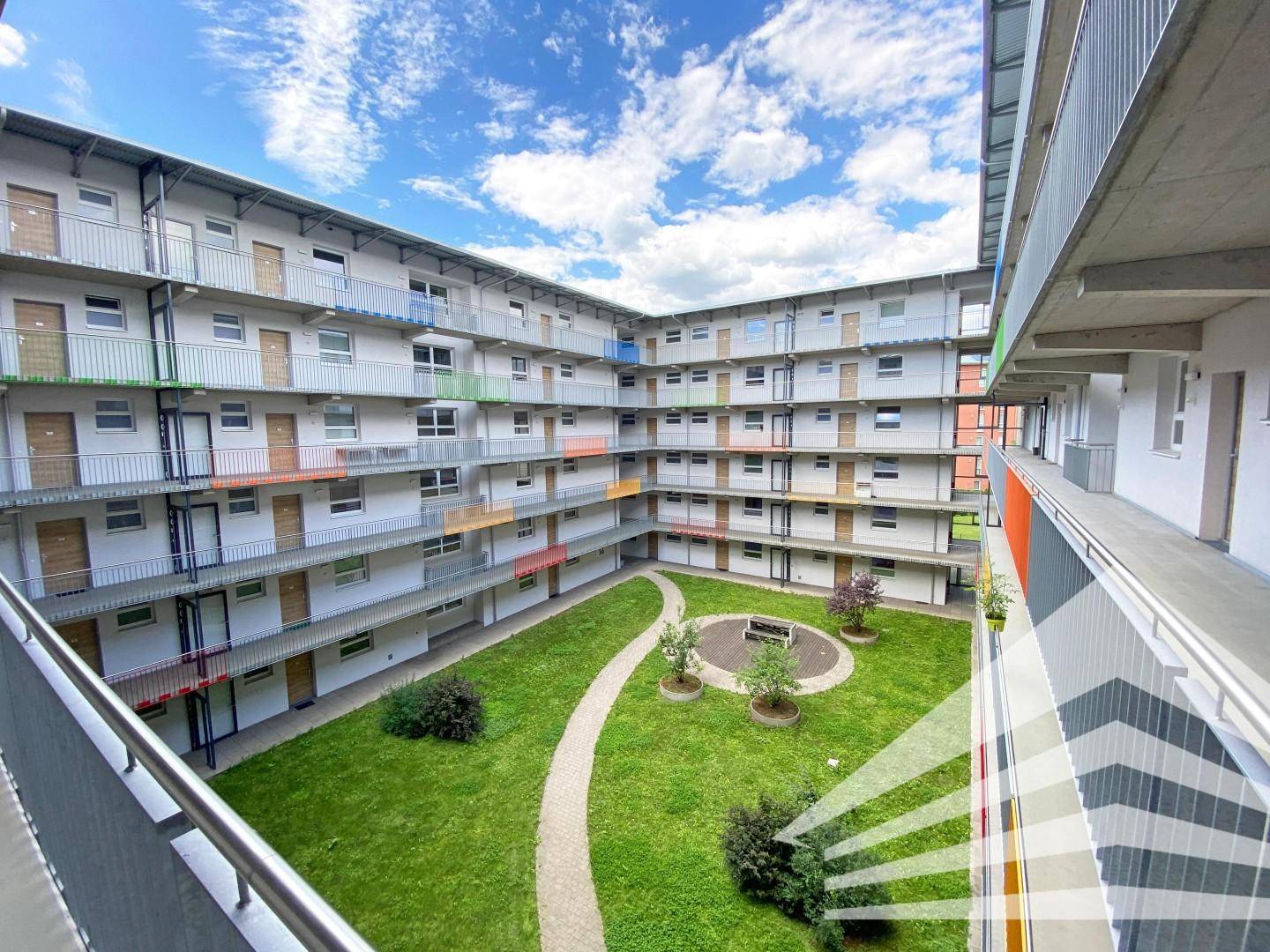 Innenhof eines modernen Wohnkomplexes mit gepflegter Rasenfläche und umlaufenden Balkonen.