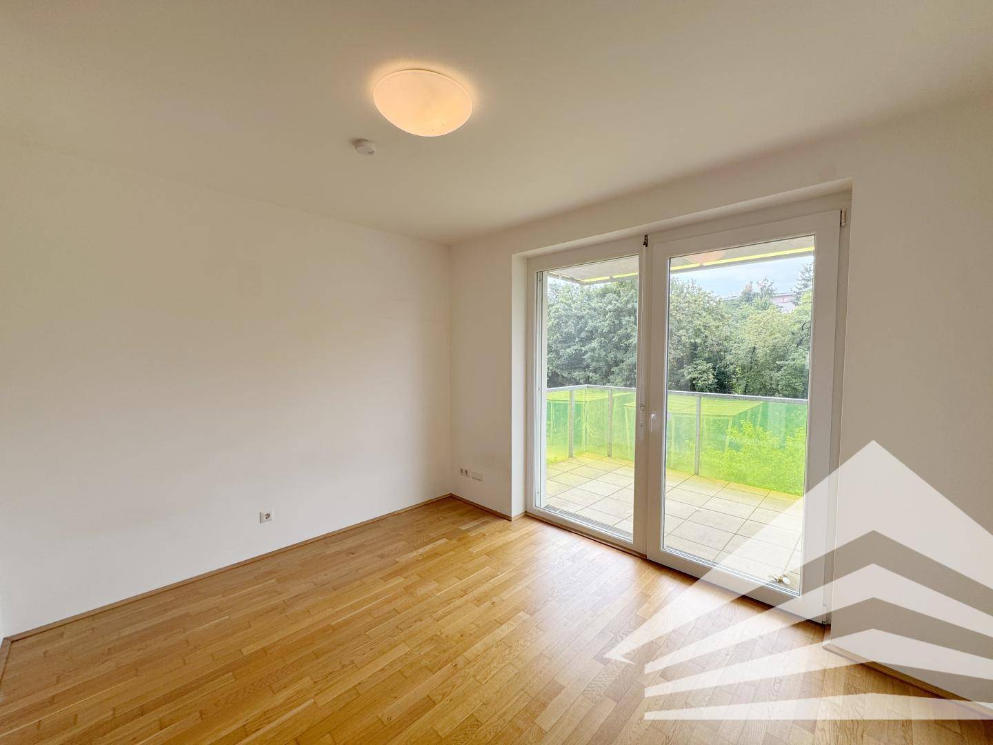 Helles Zimmer mit Holzboden und großem Fenster, das Zugang zu einer Terrasse bietet.