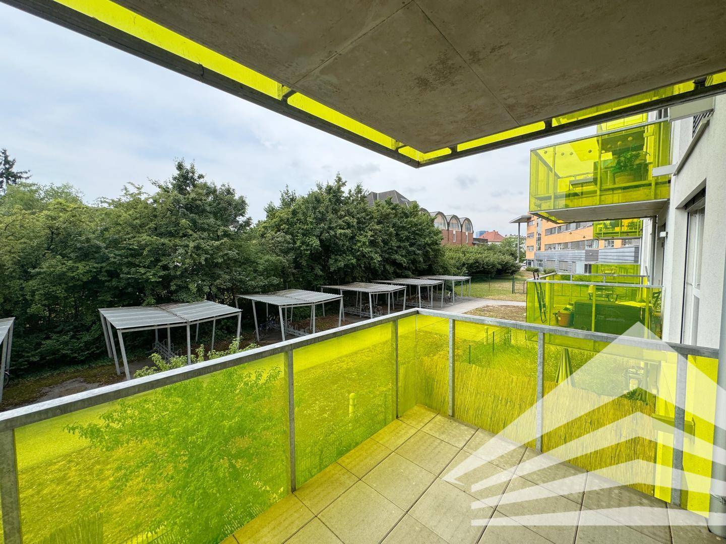Geräumiger Balkon mit farbigen Glasgeländern und Ausblick ins Grüne.