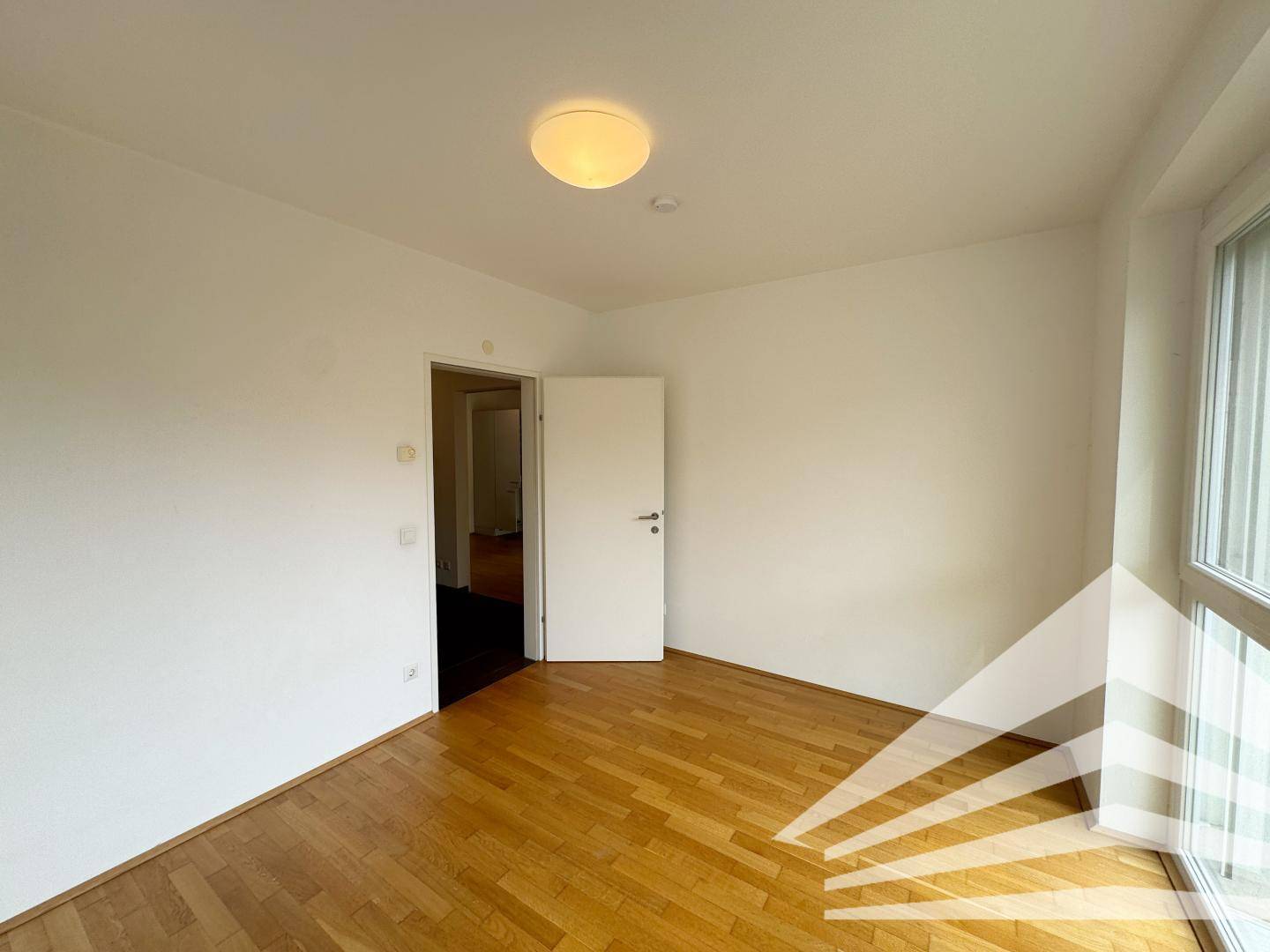Leeres Zimmer mit Parkettboden und weiß gestrichenen Wänden, bereit zur Einrichtung.