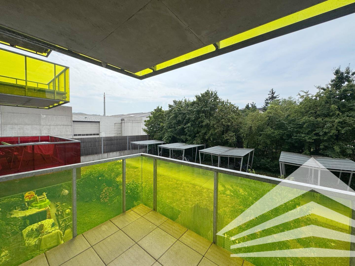 Balkon mit gelben Glasgeländern und Blick auf Bäume und umliegende Gebäude.