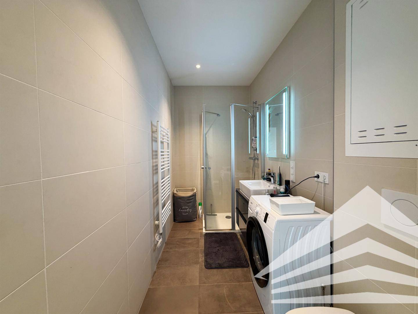 Modernes Badezimmer mit Dusche, Doppelwaschbecken und Waschmaschine.