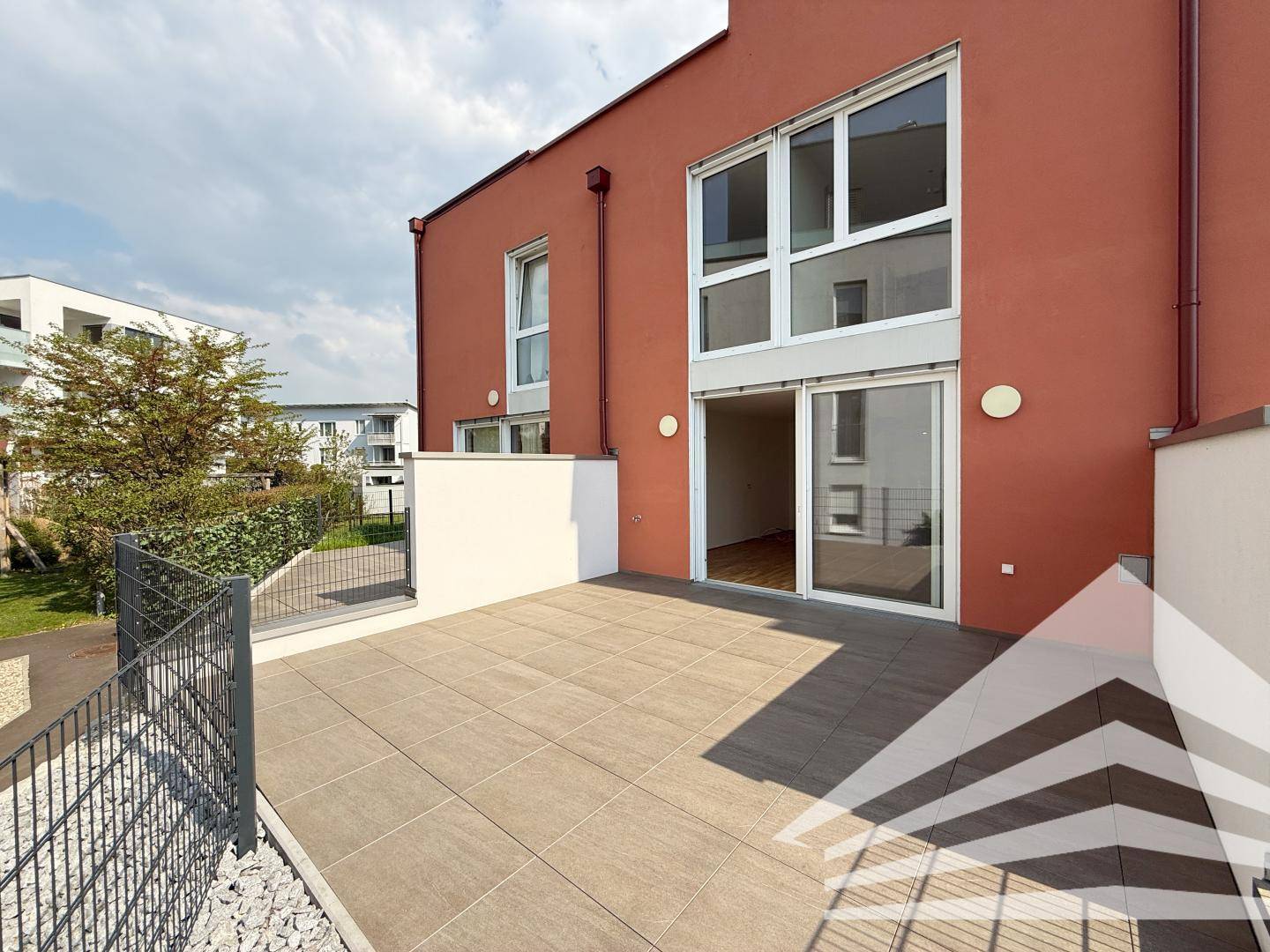 Helle geflieste Terrasse mit Zugang zum Gebäude und Blick auf die gepflegte Außenanlage.