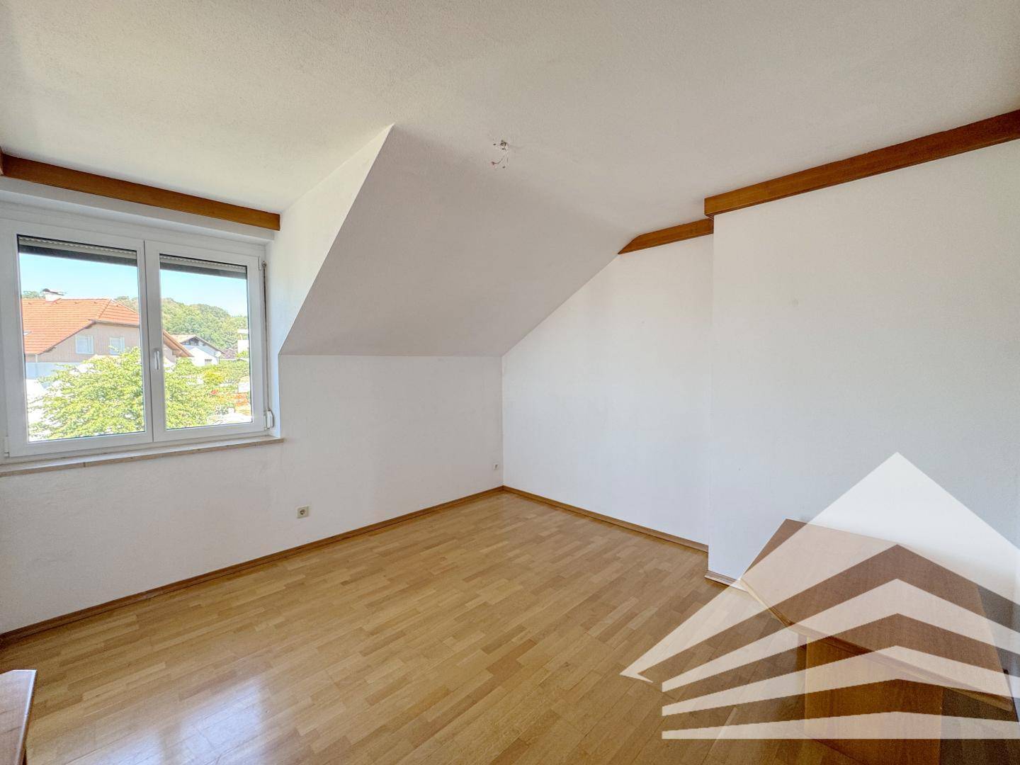 Helles Schlafzimmer mit Holzboden, Dachschräge und Fenster mit Blick ins Grüne.