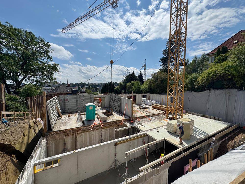 Baustelle mit im Bau befindlichem Fundament und Kellerwänden, umgeben von Baukränen.