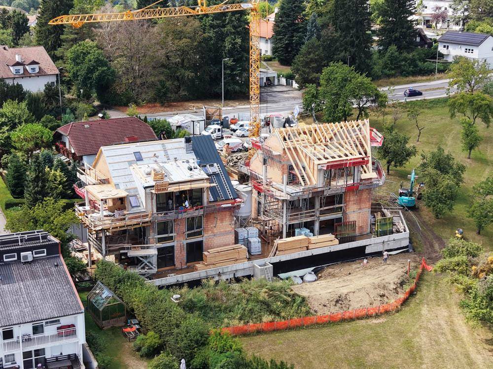 Luftaufnahme einer Baustelle mit zwei im Bau befindlichen Gebäuden und einem großen Baukran.