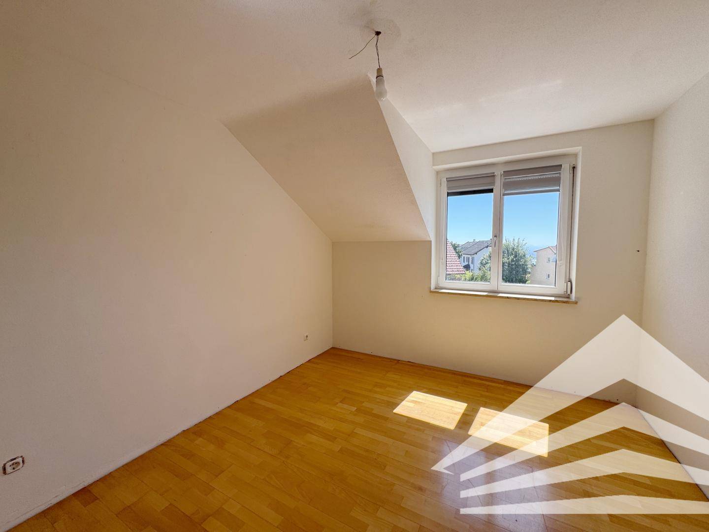Helles Schlafzimmer mit Holzboden, Dachschräge und Fenster mit Rollladen.