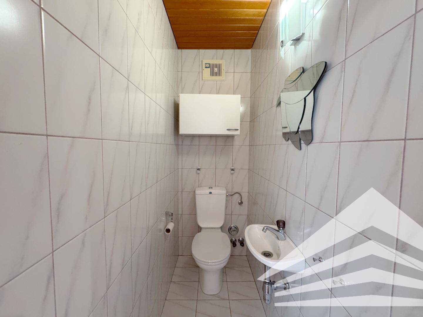 Separates WC mit Fliesen, Toilette und kleinem Waschbecken.