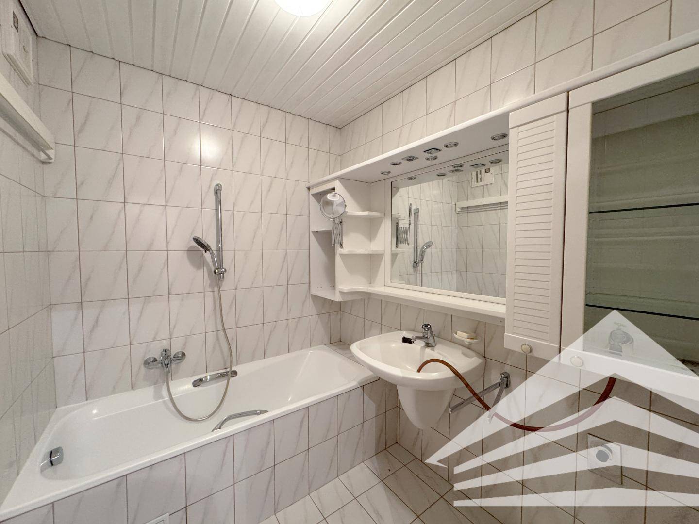 Gefliestes Badezimmer mit Badewanne, Waschbecken und Spiegelschrank.