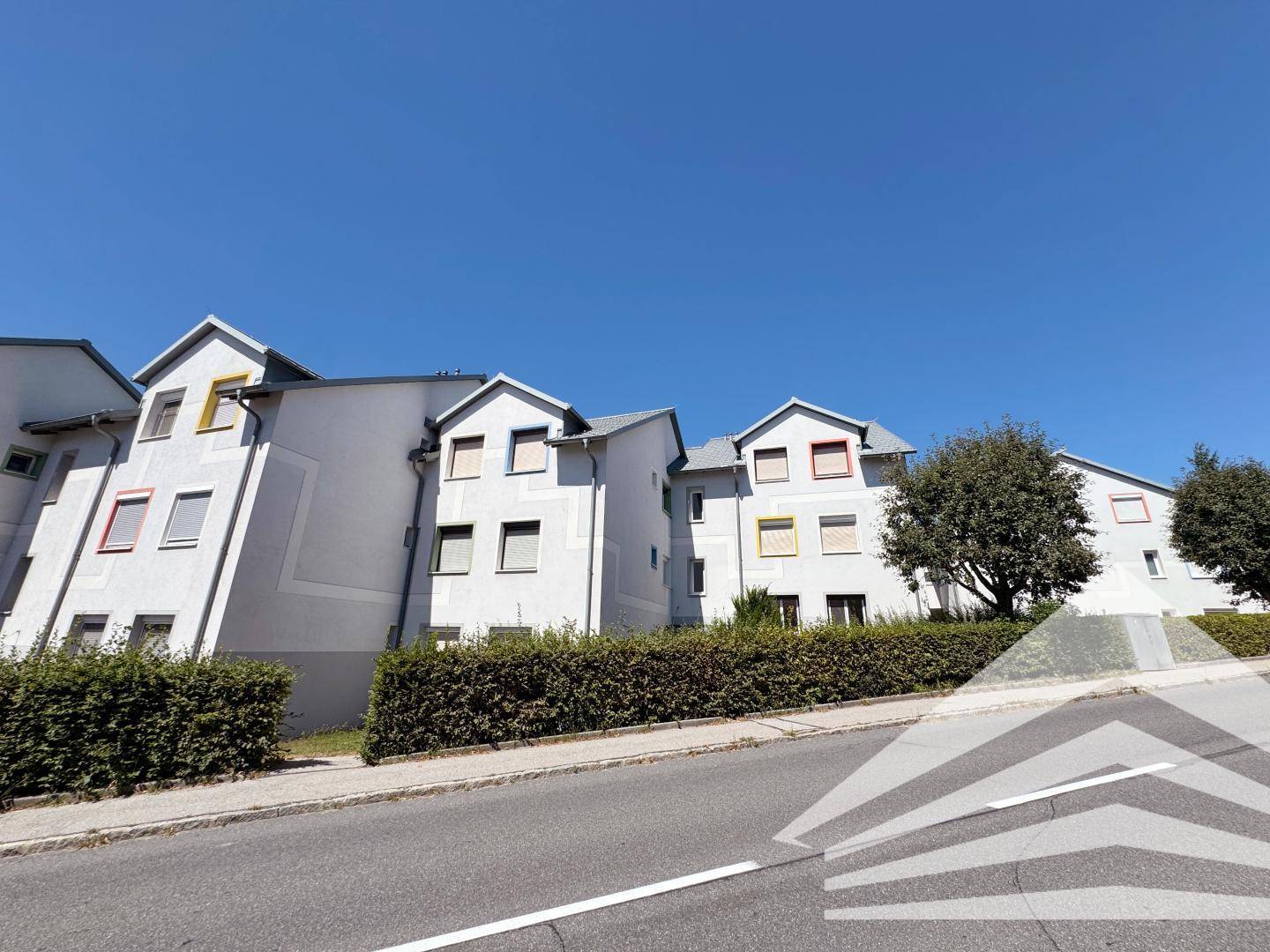 Wohngebäude mit gepflegter Hecke und farbigen Akzenten an den Fenstern.