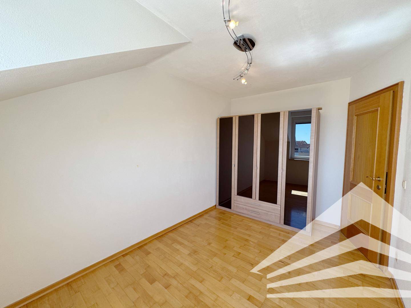 Helles Schlafzimmer mit Holzboden, Einbauschrank und Blick nach draußen.