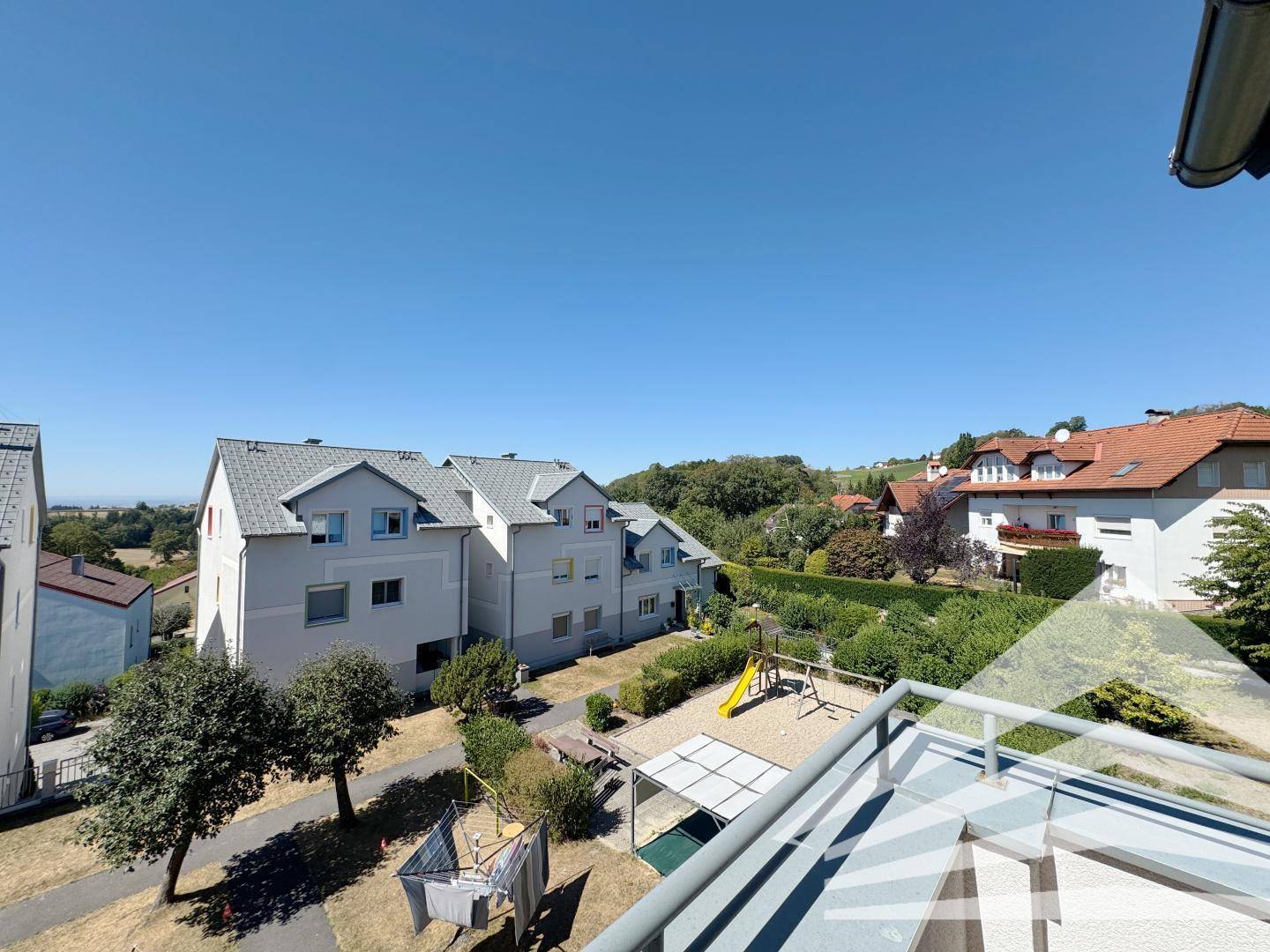 Sonniger Balkon mit Blick auf einen Spielplatz und die umliegende Wohnsiedlung.