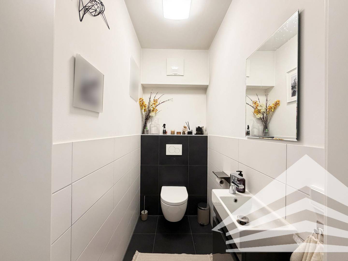 Modernes Gäste-WC mit Wand-WC, kleinem Waschbecken und dunklen Akzentfliesen.