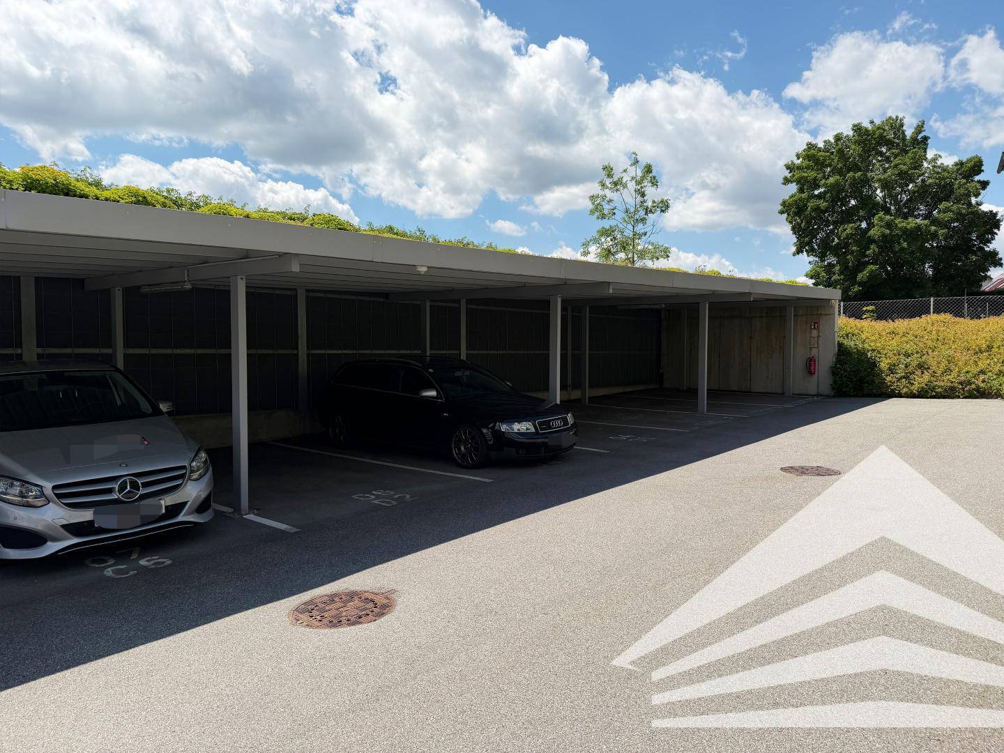Überdachte Parkplätze im Freien mit begrüntem Dach und mehreren Fahrzeugen.
