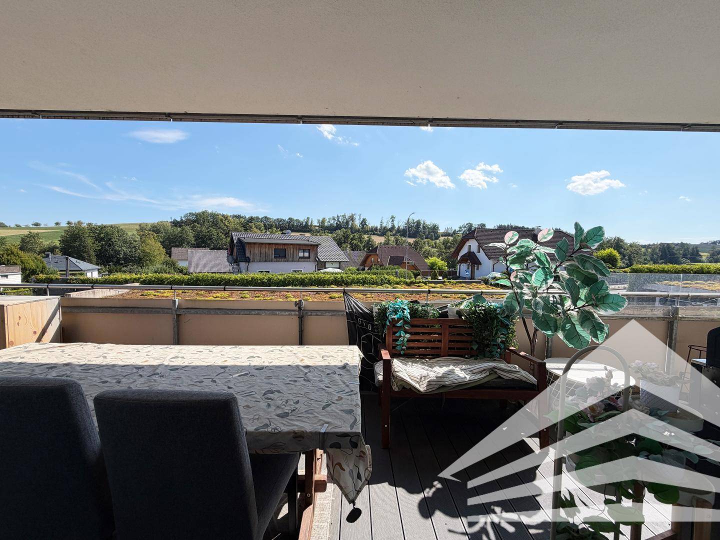 Weitläufiger Blick vom Balkon über die grüne Landschaft und umliegende Häuser.