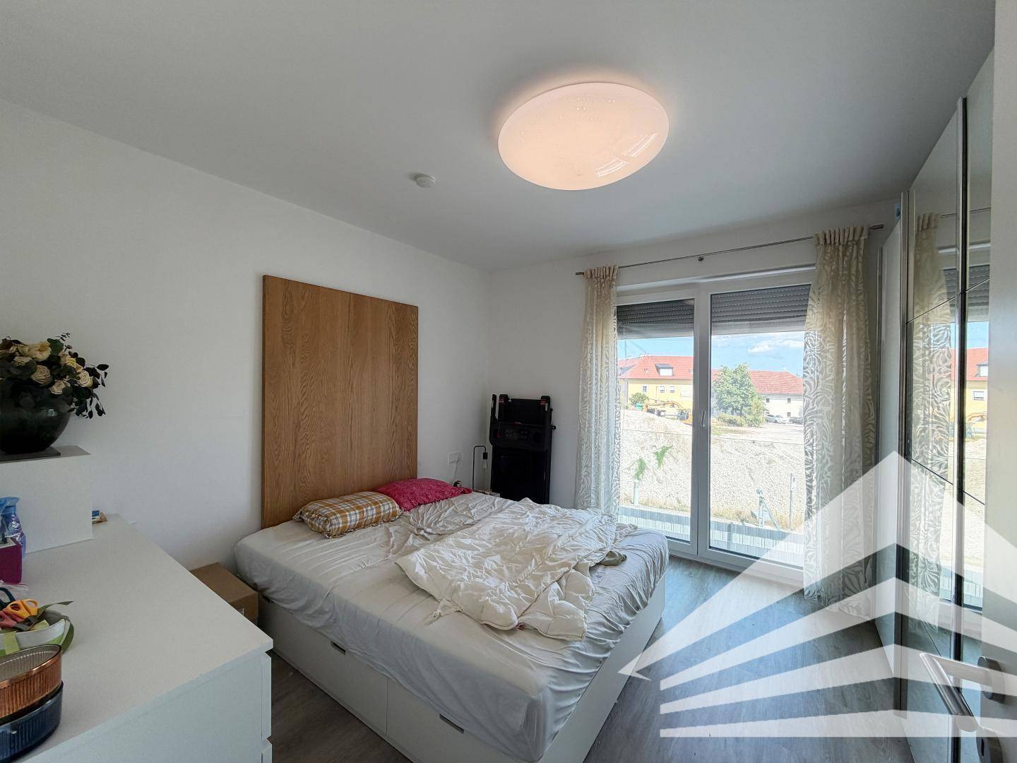 Schlafzimmer mit Doppelbett, Holz-Kopfteil und Zugang zu einem Balkon.