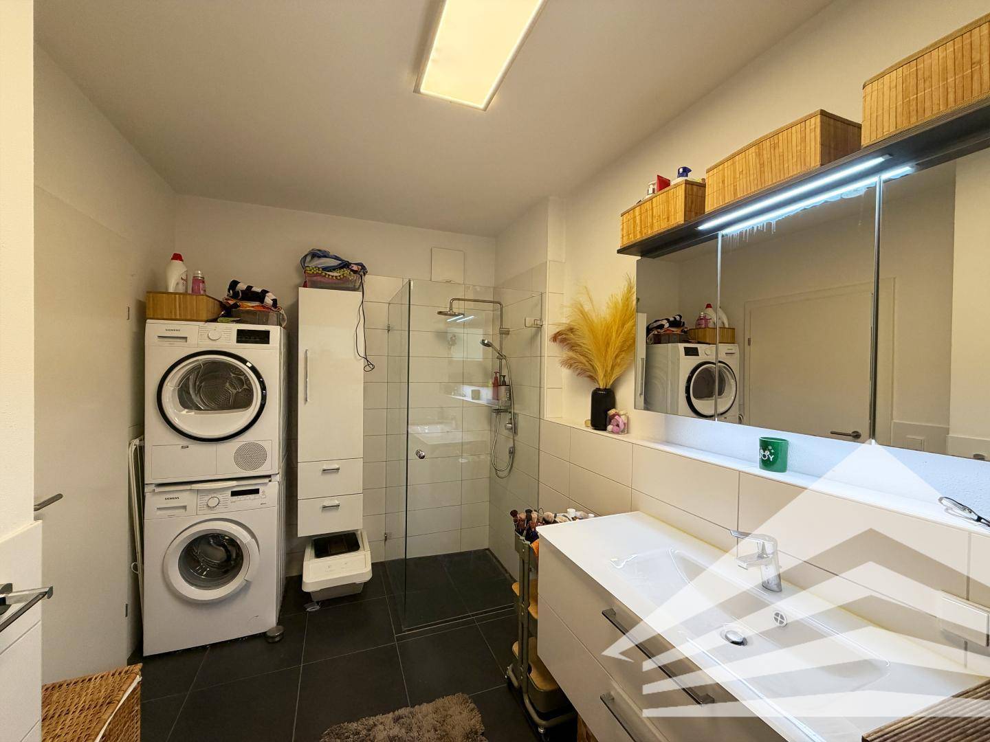 Badezimmer mit Waschmaschine, Trockner, Duschkabine und modernem Waschtisch.