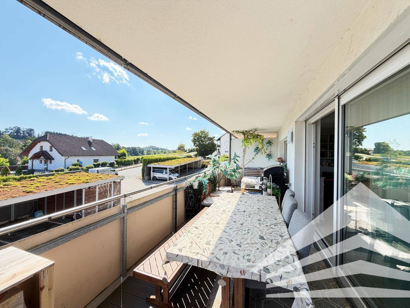 Geräumiger Balkon mit Esstisch und Sitzgelegenheiten, umgeben von grüner Landschaft und Häusern.