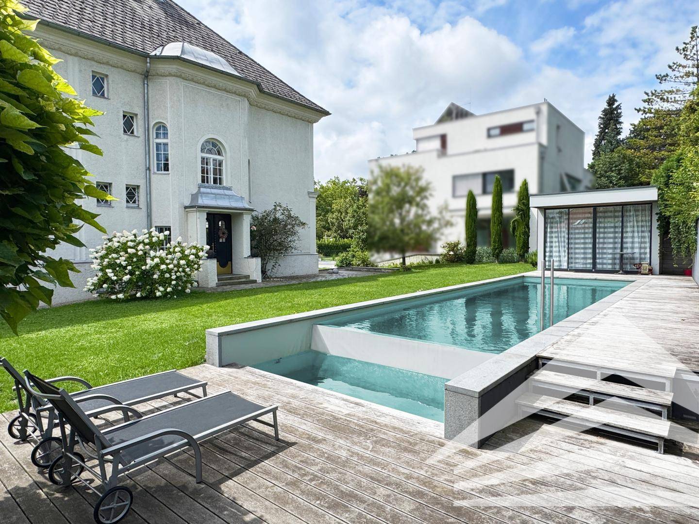 Außenbereich mit modernem Pool, Holzdeck, Liegestühlen und Blick auf die umliegende Bebauung.