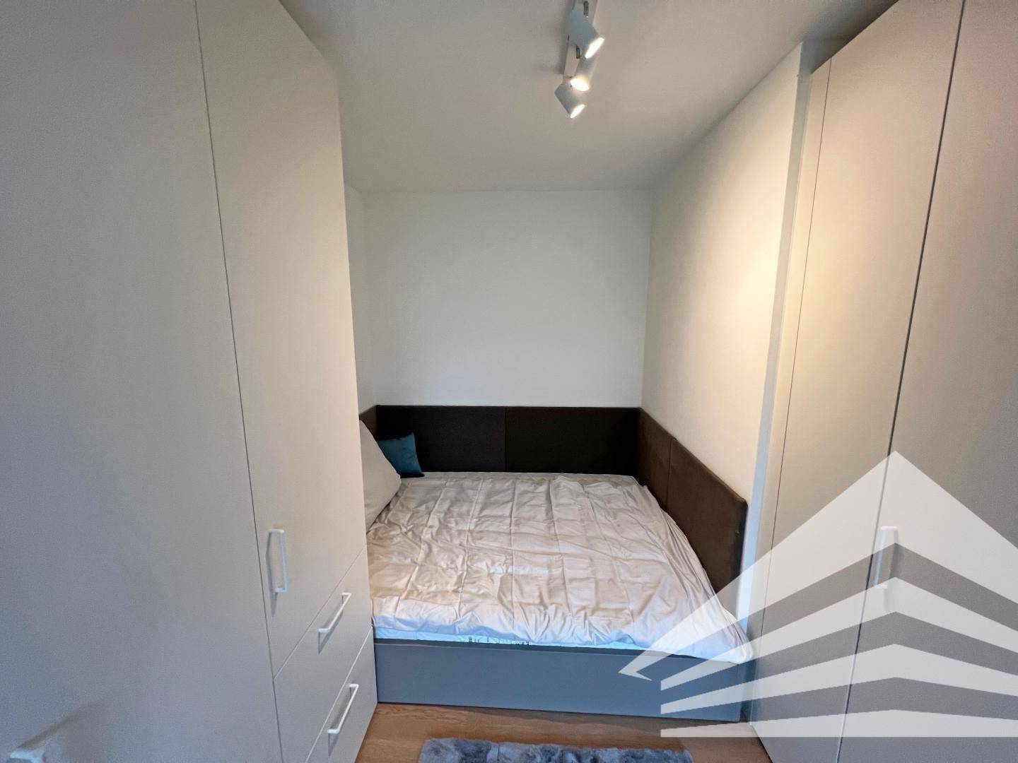 Kompaktes Schlafzimmer mit Doppelbett, integriertem Kopfteil und Einbauschränken.